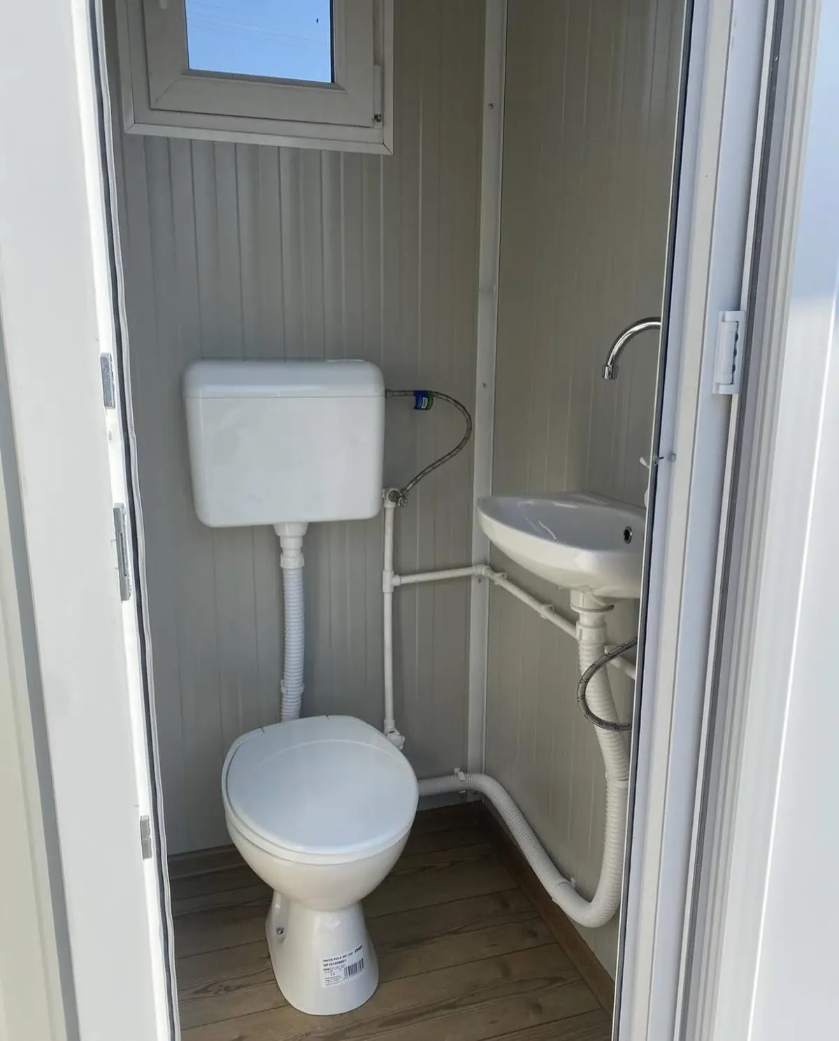 Inside a flushing restroom cabin with a tank toilet and a small wall sink