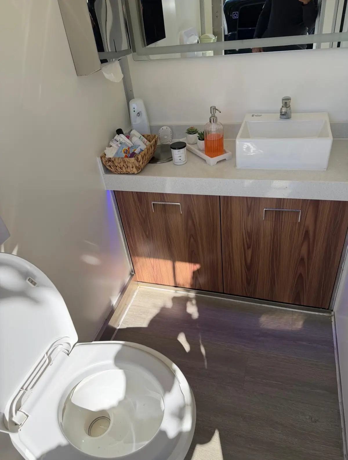 Wood-cabinet vanity with a white sink inside a luxury restroom trailer