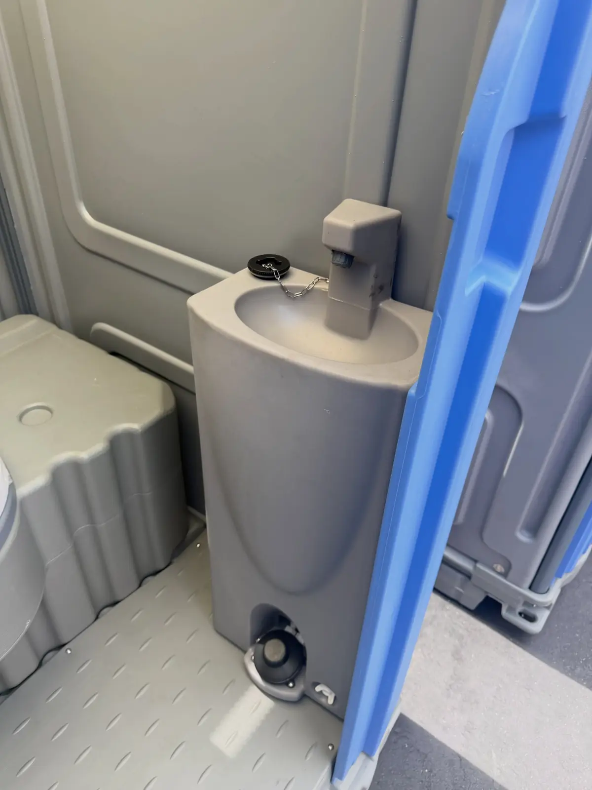 Grey built-in hand sink with a foot pump inside a portable toilet