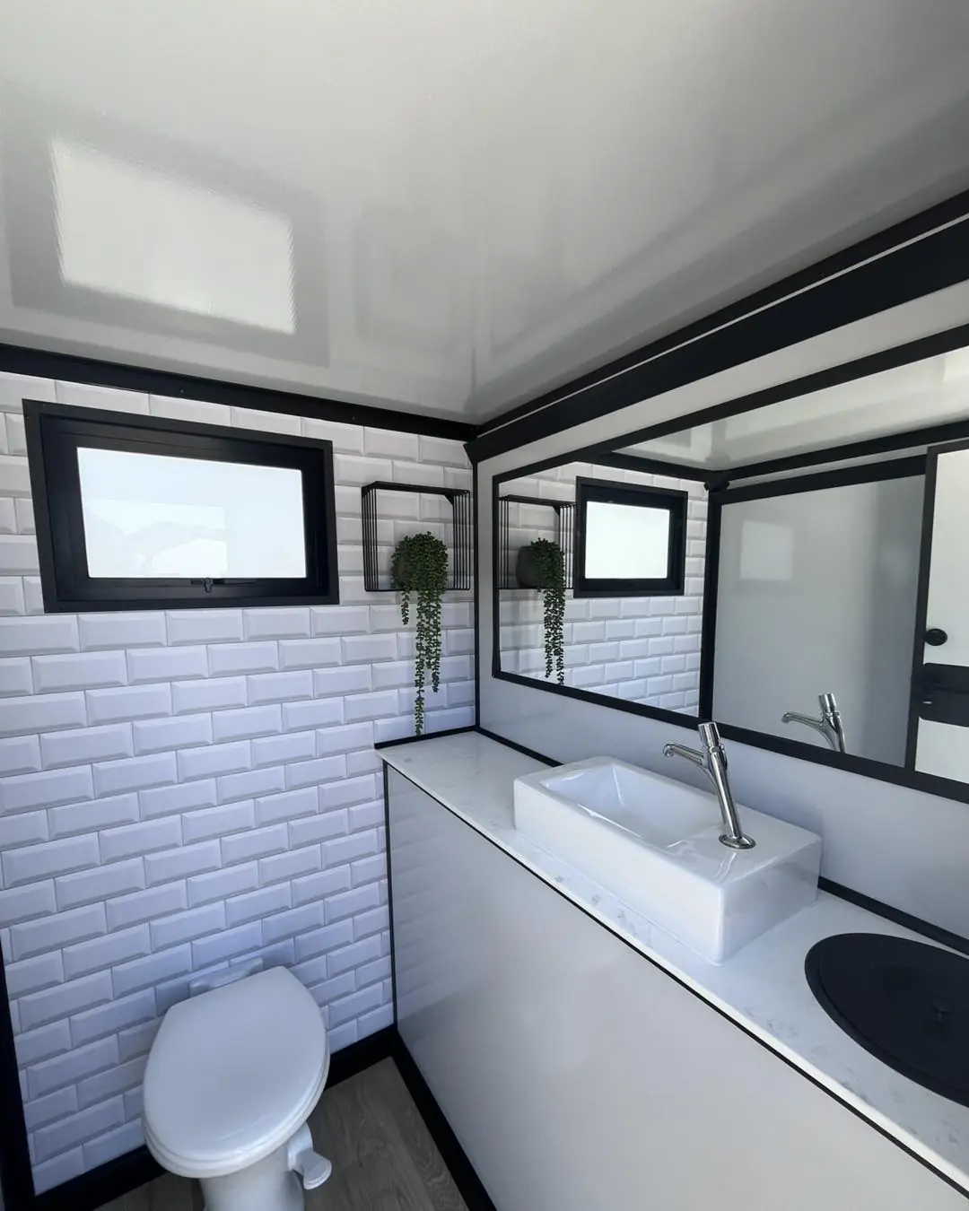 Restroom trailer stall with white tile walls, a toilet and a sink