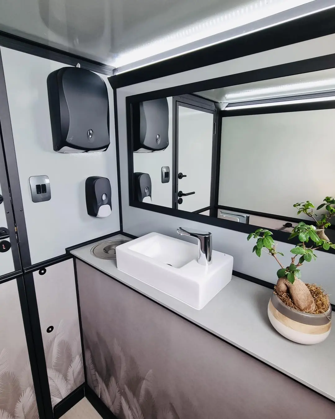 Restroom trailer vanity with a white sink, mirror, soap and towel dispensers