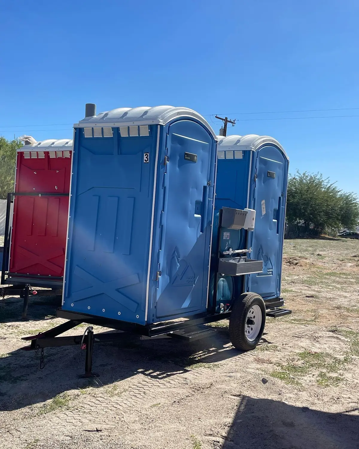 Porta potties loaded on a towable trailer in a gravel yard